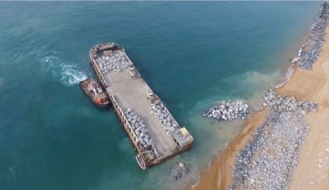 Aerial view of a TMTLLS barge unloading stone at the shore